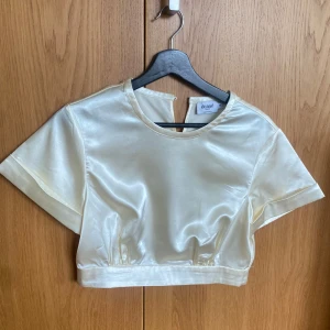 Krämvit croppad satintopp från NAKD x Danae - Säljer en krämvit croppad topp i satin från NAKD x Danae. Toppen har korta ärmar och rund halsringning. Perfekt för fest eller andra finare tillställningar. Använd endast 1 gång (som ny). Storlek 38 (sitter som en S/M). Nypris 699kr men är nu slutsåld efter hög efterfrågan vid släppet :)
