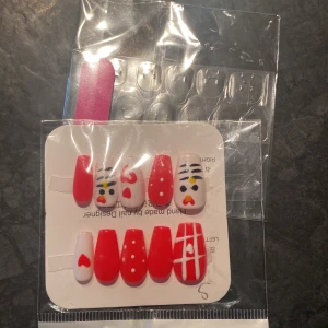 Röda och vita lösnaglar med mönster - Säljer ett set lösnaglar i rött och vitt med olika mönster som hjärtan, prickar och linjer. Några naglar har även söta ansikten målade. Perfekt för dig som vill ha en unik och färgglad nageldesign.