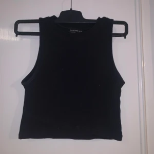 Svart croppad linnetopp från Stradivarius - Säljer en svart croppad linnetopp från Stradivarius. Toppen är ribbad och ärmlös med rund halsringning. Perfekt att styla till olika outfits och enkel att matcha med både jeans och kjol.