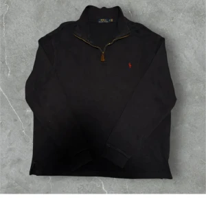 Marinblå långärmad tröja med dragkedja från Polo Ralph Lauren - Klassisk marinblå långärmad tröja från Polo Ralph Lauren med halv dragkedja och liten röd logga broderad på bröstet. Hög krage och ribbade muddar vid ärmslut. Perfekt för en stilren och avslappnad look.