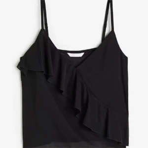 Svart volanglinne från H&M - Säljer ett svart linne från H&M med smala axelband och snygg volangdetalj framtill. Toppen är i storlek M men passar även S, den är tillverkad i ett mjukt, tunt material som är perfekt under sommaren. Aldrig använt toppen.