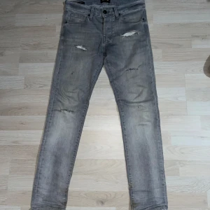 Grå jeans från Jack & Jones - Säljer ett par grå jeans från Jack & Jones med sköna slitna detaljer och klassisk femficksdesign. Jeansen har slim/glenn passform och raka ben. Perfekta för en avslappnad stil och funkar året runt. Jeansen är i bra skick och har lite av en tvättad look. Storleken är W29 L29. Skriv gärna vid minsta fråga, pris kan diskuteras.