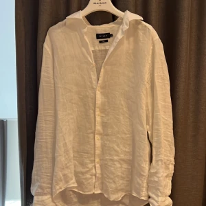 Vit linneskjorta från Riley - Säljer en klassisk vit skjorta i linne från Riley. Skjortan har lång ärm, knappar framtill och en avslappnad passform. Perfekt för varma dagar eller en stilren look. Snygg att bära både öppen och knäppt. Grymt skick nypris 800