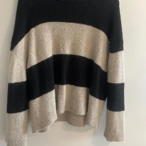 Randig stickad tröja från Gina Tricot - Mysig stickad tröja från Gina Tricot i storlek L. Tröjan har breda svarta och beige ränder, lång ärm och avslappnad passform. Perfekt för kyliga dagar och enkel att styla med jeans eller kjol.