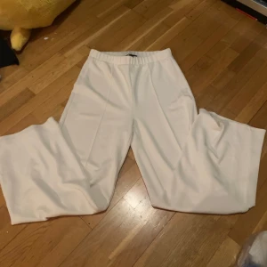 Vita vida byxor från Vero Moda - Säljer ett par vita vida byxor från Vero Moda med resår i midjan. Byxorna har en lös passform och är tillverkade i ett mjukt material som känns bekvämt mot huden. Perfekta för en stilren och avslappnad look.