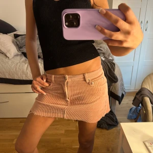 Rosa manchesterkjol med rå kant - Säljer en ljusrosa minikjol i manchester med rå kant nertill. Kjolen har klassiska jeansdetaljer som fickor fram och bak samt dragkedja och knapp framtill. Perfekt för dig som gillar en trendig och avslappnad stil.