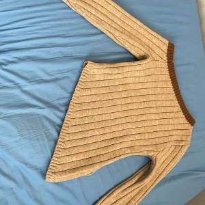 Beige ribbstickad tröja från SHEIN - Säljer en beige ribbstickad tröja från SHEIN i storlek M. Tröjan har långa ärmar och en brun ribbad kant vid halsen. Perfekt för lager-på-lager och enkel att matcha med olika outfits.