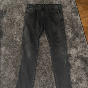 Svarta Replay jeans slim fit - Säljer ett par svarta jeans från Replay med klassisk femficksdesign och snygga detaljer på bakfickorna. Jeansen har rak passform och är tillverkade i mjukt denimtyg. Perfekta för dig som gillar stilrena och tidlösa jeans.