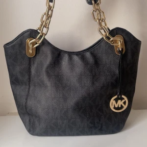 Michael kors tote bag - Priset kan diskuteras!!! Snygg svart axelväska från Michael Kors med guldfärgade kedjor som handtag och MK-logga som detalj. Väskan har diskret MK-mönster i materialet och är rymlig, perfekt för vardagsbruk. Klassisk och stilren design. 😁