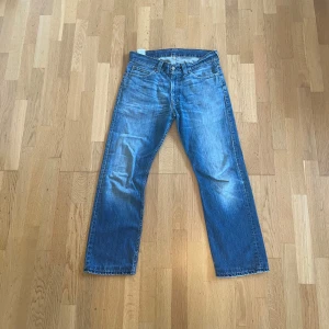 Levi's 506 blå jeans straight fit - Klassiska blå Levi's 506 jeans med rak passform och normal midja. Jeansen har fem fickor, knappgylf och snyggt slitna detaljer framtill och baktill. Perfekta för en avslappnad och tidlös stil. Passar som 34/32