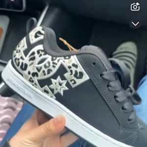 Svarta DC sneakers med leopardmönster - Snygga svarta DC sneakers med vit sula och coola leopardmönstrade detaljer på sidorna. Skorna har snörning och en stor DC-logga i vitt och beige med stjärndetalj. Perfekta för dig som vill sticka ut med din streetstyle. Lite liten storlek!