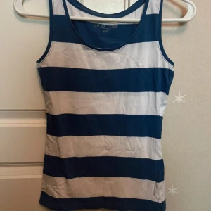 Randig linnetopp från Reaction - Snygg ärmlös linnetopp från Reaction i marinblått och vitt med breda horisontella ränder. Perfekt för sommaren med sin klassiska look och bekväma passform. Tillverkad i mjuk bomull som känns skön mot huden.