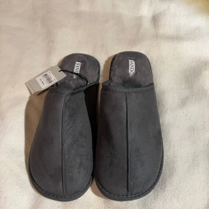 Gråa tofflor från Sandö, storlek 44/45 - Mysiga gråa tofflor från Sandö med mjuk pälsliknande insida och ovandel i syntetmaterial. Helt nya och aldrig använda sitter fortfarande tagg kvar! Ny pris 499kr 