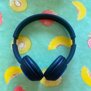 Trådlösa hörlurar bluetooth  - Bilderna visar ett par svarta over-ear hörlurar med blå detaljer. Hörlurarna har vadderade kåpor och justerbart huvudband. De har uttag för laddning och ljudkabel. Perfekt för dig som vill lyssna på musik eller poddar med stil och komfort. Nypris 799 säljes för 200kr