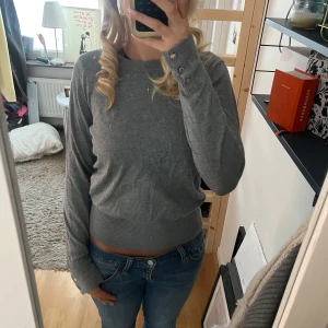 Grå tröja från Holly & Whyte - Snygg grå tröja från Holly & Whyte Långärmad modell med knappar i guld på ärmsluten. 