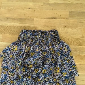 Blommig volangkjol från H&M - Supersöt kort volangkjol från H&M med blommigt mönster i lila, blått, gult och svart. Kjolen har smock i midjan och flera lager volanger som ger en riktigt flowy känsla. Perfekt för dig som gillar färg och mönster! Om ni är intresserad av nått mer från min sida säg till! Så kan jag lägga ihop de i samma