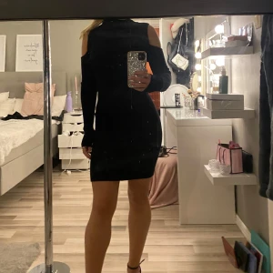 Svart tight klänning med cut out - Snygg svart kortklänning med tight passform och trendiga cut out-detaljer på axlarna. Hög hals och långa ärmar. Klänningen är stickad och passar perfekt till vintern.