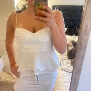 Vit linnetopp med volang från Zara - Supersöt vit linnetopp från Zara med smala axelband som knyts på axlarna och volang nertill.      Obs: märken på insidan och utsidan av armhålorna samt på insidan av ryggen. Passar bättre till storlek S-M