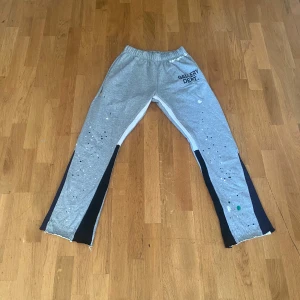 Grå mjukisbyxor Gallery Dept. L - Snygga grå mjukisbyxor från Gallery Dept. med svart och vit panel längs benen och coola färgstänk som ger en unik vibe. Byxorna har resår i midjan, snörning och råa benslut. Tillverkade i 100% bomull för maximal komfort.