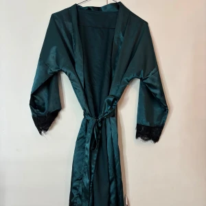 Mörkgrön morgonrock med spets - Snygg mörkgrön morgonrock i satinliknande material med knytband i midjan. Svarta spetsdetaljer vid armarna och vid slutet av morgonrocken. Den är från shein och skulle tro det är storlek XS-S. Aldrig använd så nyskick