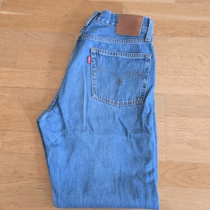Levi's 501 ljusblå jeans W26 L28 - Klassiska Levi's 501 jeans i ljusblå denim. Rak passform med fem fickor, knappgylf och ikonisk läderpatch bak i midjan. Perfekta för dig som gillar tidlös stil och vill ha ett par riktigt snygga jeans i bomull.