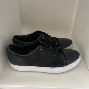 Svarta sneakers med vit sula - Svarta sneakers med snygg vit platt sula och klassisk snörning. Skorna har en rund tå och är tillverkade i mocka och skinn, vilket ger dem en cool och stilren vibe. Perfekta för dig som gillar enkel och tidlös design.