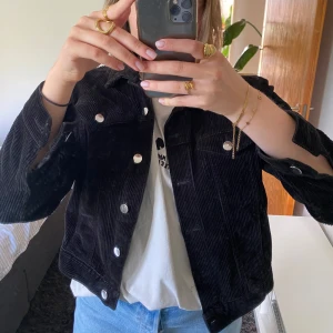 Svart manchesterjacka från Monki - Svart manchesterjacka från Monki med klassisk krage, knappar framtill och två bröstfickor. Perfekt för dig som vill ha en stilren och trendig look.