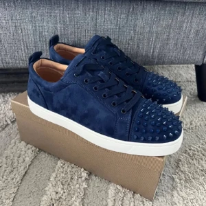 Mörkblå mocka sneakers från Louboutin - Snygga mörkblå sneakers i mocka från Christian Louboutin med vita sulor och ikonisk röd undersida. Skorna har snörning och coola nitar på tån för en edgy vibe. Perfekta för dig som vill sticka ut med exklusiv streetstyle.