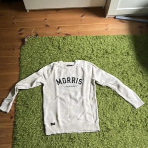 Vit stickad tröja Morris Company - Snygg vit stickad tröja från Morris Company i storlek small. Tröjan har rund hals, långa ärmar och ett broderat Morris Company-tryck framtill. Ribbstickade muddar vid ärmslut och nederkant ger en clean look. Perfekt för dig som gillar klassisk stil med en modern touch.