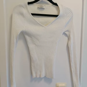 Vit ribbad v-ringad tröja Chiquelle - Supersnygg vit ribbad tröja från Chiquelle med v-ringad hals och långärmade smala ärmar. Tröjan är tight i passformen och gjord i mjuk stickad bomull som sitter perfekt. Perfekt att styla med jeans eller kjol för en clean look.