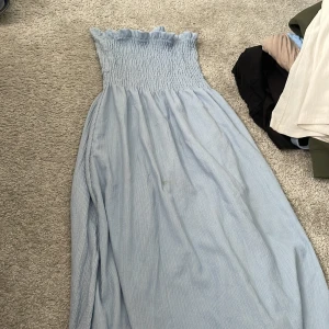 Ljusblå långklänning från H&M XS - Supersöt ljusblå långklänning från H&M i storlek XS. Klänningen har smock upptill med volangkant och är axelbandslös. Materialet är mjukt och luftigt, perfekt för varma dagar. Passformen är loose och klänningen har en flowy siluett. Kan användas som långkjol. 