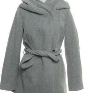 Grå kappa med huva från Amisu  - Snygg grå kappa från Amisu med stor huva och knytskärp i midjan. Klassisk och stilren modell som ger en chill men ändå uppklädd vibe. Perfekt för kyliga dagar och enkel att matcha med olika outfits.