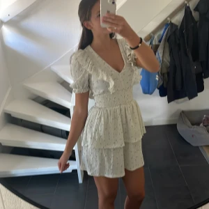 Blommig volangklänning Gina Tricot XS - Supersöt kortklänning från Gina Tricot i ljus grönt med små blommor och volanger. Klänningen har v-ringning, puffiga kortärmar och smock i midjan. Materialet är lätt och känns som bomull, perfekt för sommarens alla tillfällen. Två lager volanger ger extra flow.