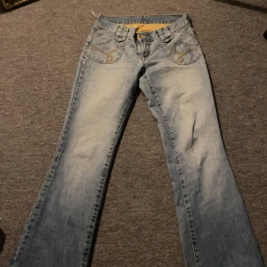 Ljusblå bootcut jeans med brodyr - Snygga ljusblå jeans från Freedom med bootcut passform. Jeansen har dekorativa broderier i gult på både fram- och bakfickor samt broderad logga bak. Klassisk femficksmodell i mjukt denimtyg, perfekt för dig som gillar retrovibbar.