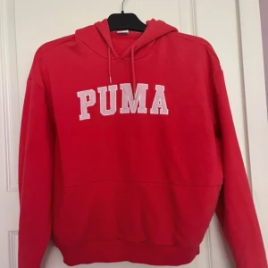 Röd hoodie från Puma med tryck - Röd hoodie från Puma i storlek XS med stort vitt PUMA-tryck på bröstet. Klassisk huva med dragsko och ribbade muddar. Perfekt för en chill och sportig look. Mjuk bomullsblandning som är skön att ha på sig.