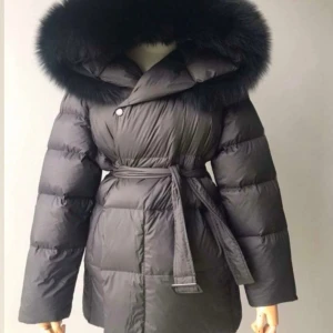 Furstockholm jacka - Säljer en svart pufferjacka med stor fluffig huva med ÄKTA RÄVPÄLS. Jackan har bälte i midjan för snygg passform och är quiltad för extra värme. Perfekt för kalla dagar och har långa ärmar. Stilren och trendig look. Korta modellen