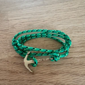 Grönt armband med ankare från Blvckout - Snyggt armband med grön och svartmönstrad rep och ett stilrent guldfärgat ankare som lås. Perfekt accessoar för dig som gillar marina vibes och vill sticka ut med färg. Ny pris 399