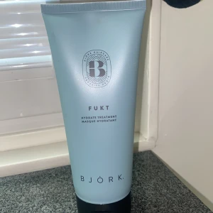 BJÖRK Fukt Hydrate Treatment - En ljusblå tub med BJÖRK Fukt Hydrate Treatment, en återfuktande hårmask. Tuben har svart lock och stilren design med silverdetaljer. Perfekt för dig som vill ge håret extra fukt och vård.