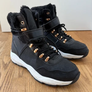 Svarta vinterkängor  - Svarta vinterkängor från Linear med fluffig fuskpäls runt skaftet, guldfärgade detaljer och grov vit sula. Skorna har snörning, kardborreband och är vattentäta. Använda ett fåtal gånger men i väldigt bra skick, storlek 38.