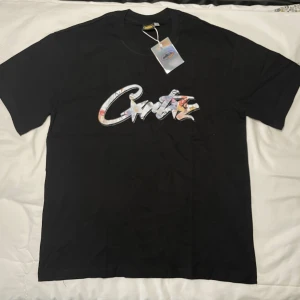 Corteiz t-shirt - Svart t-shirt från Corteiz med stort, färgglatt logotryck på bröstet i graffiti-stil. Klassisk rund hals och korta ärmar. Materialet är mjuk bomull som känns skönt mot huden. Perfekt för dig som gillar streetwear och vill sticka ut med en cool detalj. Finns två 