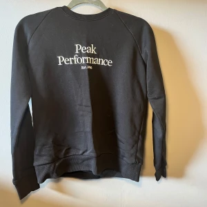 Svart Peak Performance sweatshirt S - Svart sweatshirt från Peak Performance i storlek S. Tröjan har klassisk rund hals, ribbade muddar och vit logotyp på bröstet. Mjuk insida och långärmad modell, perfekt för chill dagar. Materialet är bomull och polyester.