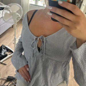 Randig blus från Hollister med knyt - Säljer en söt blus från Hollister i storlek M. Blusen är vit och blå med smala ränder, har långärmade ärmar och v-ringning med knyt framtill. Finns typ inte att få tag på längre💕skriv för mer information