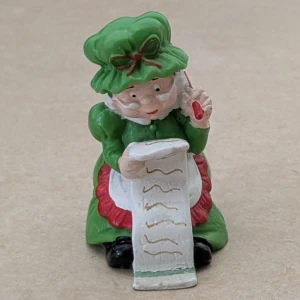 Plastfigur med julkänsla , 1980 - En färgglad figur i grönt och rött, som håller en lång lista och en penna. En dekorativ prydnadsfigur med julkänsla. 