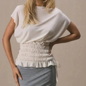 Vit omlott topp - Superfin vit topp med bred smockad midja och volangkant nertill. Toppen har korta ärmar, lös passform upptill och knytband i sidan. Har använt den 1 gång och är i väldigt bra skick