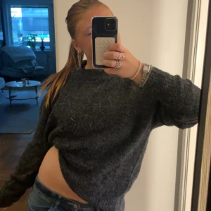 Mörkgrå stickad tröja - Mysig mörkgrå stickad tröja med loose passform och långärmade ärmar. Tröjan har en enkel design med rund hals och är perfekt för dig som gillar en chill och avslappnad stil. Passar till jeans och sneakers för en casual vibe.