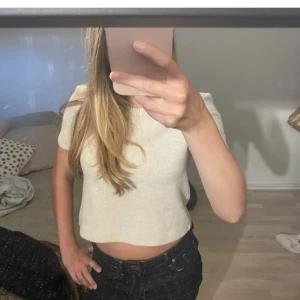 Beige croppad stickad tröja från Zara - Säljer en beige croppad stickad tröja från Zara med rund hals och korta ärmar. Tröjan har en ribbad kant vid halsen och är perfekt för dig som gillar en enkel och clean stil. Passar snyggt till både jeans och kjol. 💕