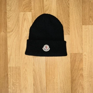 Moncler mössa i ull - LÄGG BUD PRIS KAN SÄNKAS. Svart ribbstickad mössa från Moncler med klassisk uppvikt kant och broderad logotyp framtill. Tillverkad i mjuk ull som håller dig varm och snygg under kalla dagar. Perfekt accessoar för dig som vill ha en stilren och exklusiv look. 📍Ort: Borås 📦Skick helt ny ✅orginal pris 1200kr 🚚fraktas snabbt eller mötas upp i Borås 