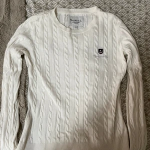 Vit kabelstickad tröja Bondelid XS - Vit kabelstickad tröja från Bondelid med rund halsringning och broderad logga på bröstet. Tröjan har lång ärm och klassisk, tidlös design som passar perfekt till jeans eller kjol. Mjuk och skön känsla tack vare bomullsmaterialet.