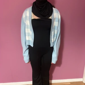 Ljusblå rutig croppad stickad väst - Superfin ljusblå croppad väst med vitt rutmönster och v-ringning. Västen är stickad och har knappar framtill. Perfekt för lager-på-lager och ger en söt och trendig look.