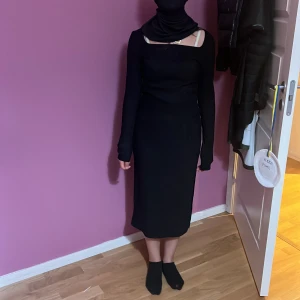 Svart långärmad klänning med slits från shein - Snygg svart långklänning med lång ärm och cool asymmetrisk halsringning. Klänningen har en slits på sidan som ger extra edge och är tillverkad i mjukt stretchigt material med 95% polyester och 5% elastan. Passformen är slim och den är helt enfärgad utan mönster.